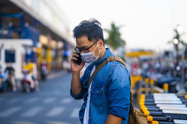 Sokakta telefon kullanırken ameliyat maskesi takan bir adam. Mikropları, zehirli dumanları ve tozu önlemek için koruyucu maske takan genç bir adamın portresi. Bakteriyel enfeksiyonun önlenmesi Corona virüsü veya Covid 19 sokaklarda ve bahçelerde.