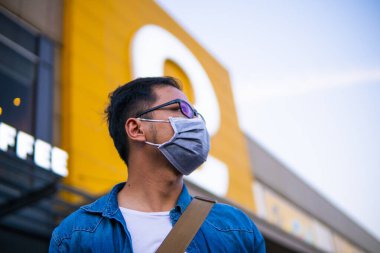 Mikropları, zehirli dumanı ve tozu önlemek için süpermarketin dışında koruyucu maske takan genç bir adamın portresi. Bakteriyel enfeksiyonun önlenmesi Corona virüsü veya Covid 19 sokaklarda ve bahçelerde.