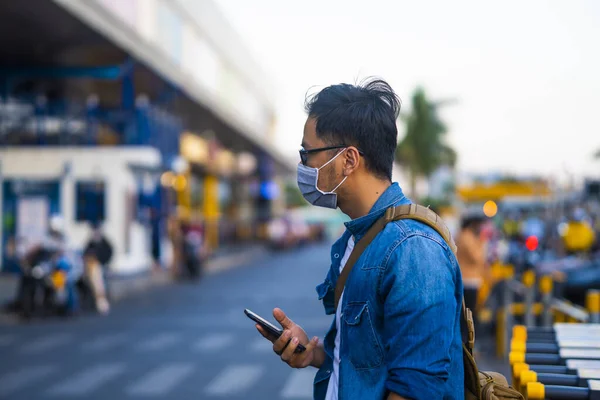 Man wearing surgical mask on street while using phone. Portrait of young man wearing a protective mask to prevent germs, toxic fumes, and dust. Prevention of bacterial infection Corona virus or Covid 19 in the air around the streets and gardens.