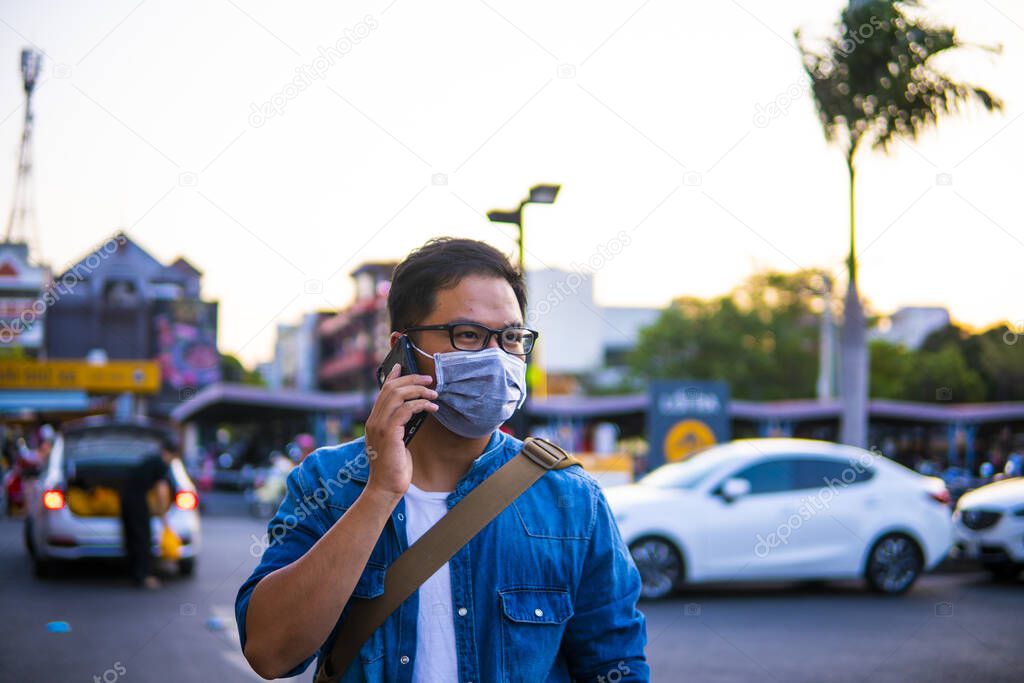 Man wearing surgical mask on street while using phone. Portrait of young man wearing a protective mask to prevent germs, toxic fumes, and dust. Prevention of bacterial infection Corona virus or Covid 19 in the air around the streets and gardens.