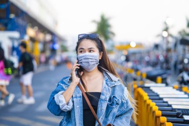 Sokakta cep telefonu kullanırken ameliyat maskesi takan genç bir kadın. Mikropları, zehirli dumanları ve tozu önlemek için koruyucu maske takan genç bir kadının portresi. Bakteriyel enfeksiyonun önlenmesi Corona virüsü veya Covid 19.