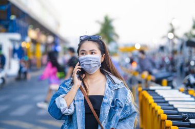 Sokakta cep telefonu kullanırken ameliyat maskesi takan genç bir kadın. Mikropları, zehirli dumanları ve tozu önlemek için koruyucu maske takan genç bir kadının portresi. Bakteriyel enfeksiyonun önlenmesi Corona virüsü veya Covid 19.