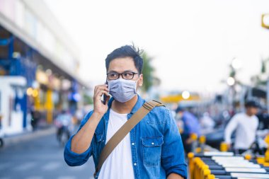 Sokakta telefon kullanırken ameliyat maskesi takan bir adam. Mikropları, zehirli dumanları ve tozu önlemek için koruyucu maske takan genç bir adamın portresi. Bakteriyel enfeksiyonun önlenmesi Corona virüsü veya Covid 19 sokaklarda ve bahçelerde.