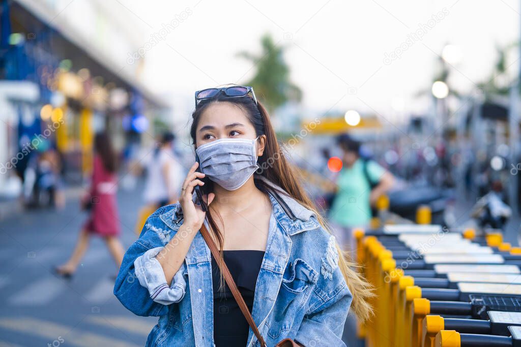 young woman wearing surgical mask on street while using mobile phone. Portrait of young woman wearing a protective mask to prevent germs, toxic fumes, and dust. Prevention of bacterial infection Corona virus or Covid 19.