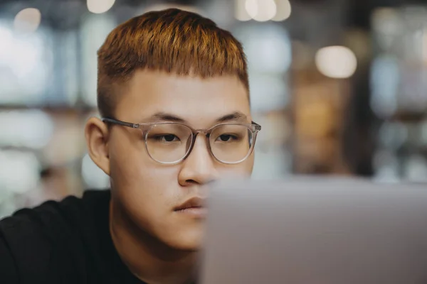 Asian young man indoors in cafe. Lifestyle concept photo with copy space. Picture with handsome guy who using protective face mask. Portrait with gray laptop