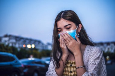 Sağlıksız Asyalı kadın Coronavirus veya Covid-19 hastalığını korumak için koruyucu maske takıp öksürüyor.
