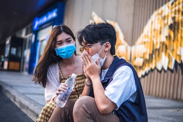 不健康なアジア人男性スニーズと咳で保護顔マスクながら女性を助けるしようとします — ストック写真