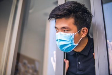 Tıbbi maskeli genç Asyalı adam evin kapısını açıyor. Coronavirus konsepti. Solunum koruması. Evde karantina.