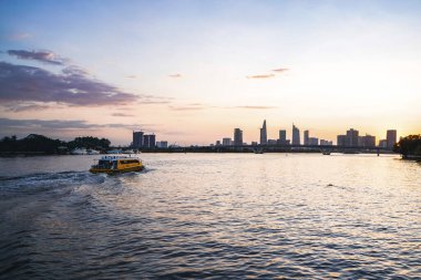 River City manzarası alacakaranlık günbatımında. Nehirde sakin suyu olan bir tekne. Bitexco kulesi olan Hochiminh şehri Saigon Vietnam şehir merkezi. Saigon nehri manzarası bulutlu ve güneşli