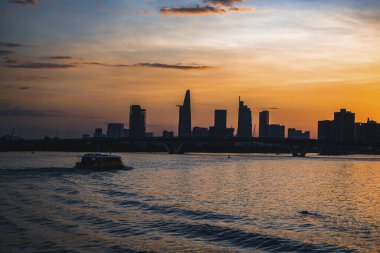 River City manzarası alacakaranlık günbatımında. Nehirde sakin suyu olan bir tekne. Bitexco kulesi olan Hochiminh şehri Saigon Vietnam şehir merkezi. Saigon nehri manzarası bulutlu ve güneşli