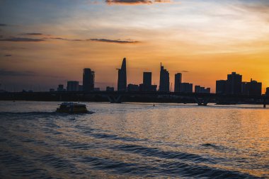 River City manzarası alacakaranlık günbatımında. Nehirde sakin suyu olan bir tekne. Bitexco kulesi olan Hochiminh şehri Saigon Vietnam şehir merkezi. Saigon nehri manzarası bulutlu ve güneşli
