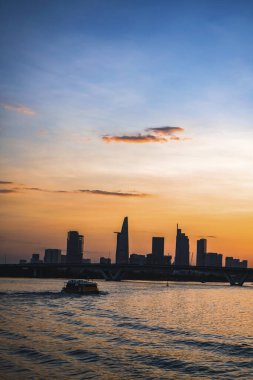 River City manzarası alacakaranlık günbatımında. Nehirde sakin suyu olan bir tekne. Bitexco kulesi olan Hochiminh şehri Saigon Vietnam şehir merkezi. Saigon nehri manzarası bulutlu ve güneşli