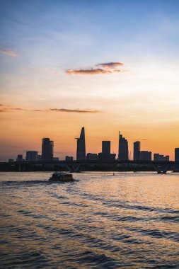 River City manzarası alacakaranlık günbatımında. Nehirde sakin suyu olan bir tekne. Bitexco kulesi olan Hochiminh şehri Saigon Vietnam şehir merkezi. Saigon nehri manzarası bulutlu ve güneşli
