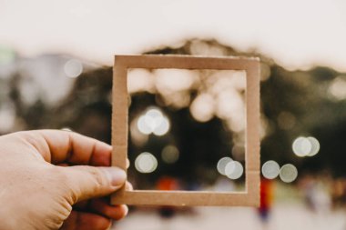 El ele tutuşan boş bir çerçeve ve doğal bir bokeh arka plan. Metin kavramı.