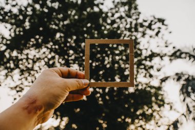 El ele tutuşan boş bir çerçeve ve doğal bir bokeh arka plan. Metin kavramı.