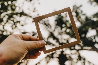El ele tutuşan boş bir çerçeve ve doğal bir bokeh arka plan. Metin kavramı.