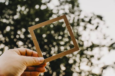 El ele tutuşan boş bir çerçeve ve doğal bir bokeh arka plan. Metin kavramı.