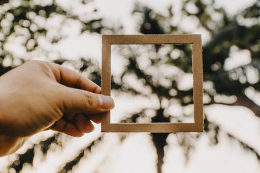 El ele tutuşan boş bir çerçeve ve doğal bir bokeh arka plan. Metin kavramı.