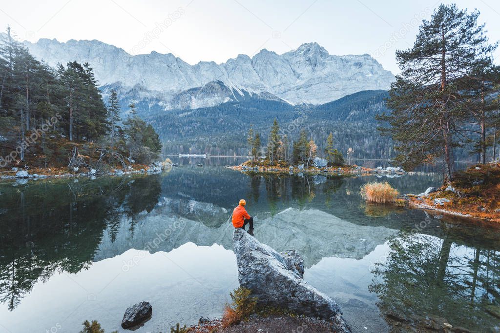Back view of a male hiker standing on rock and enjoying the views of an island at Eibsee with Germany's highest mountain in the background - Zugspitze. 