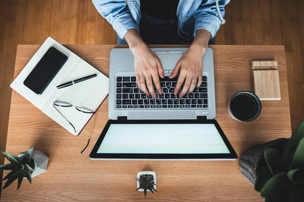 Ofis masasında çalışan bin yıllık bir kadının en iyi görüntüsü. Dizüstü bilgisayarda insan eli yazıyor. Laptop, günlük, gözlük, akıllı telefon, kalem, kahve fincanı ve çalışma masasındaki saksı bitkisi. Evden çalışan bir kadın..