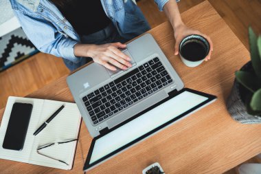 Ofis masasında çalışan ve elinde kahve fincanı tutan bin yıllık bir kadının en iyi görüntüsü. Dizüstü bilgisayarda insan eli yazıyor. Laptop, günlük, gözlük, akıllı telefon, kalem, kahve fincanı ve çalışma masasındaki saksı bitkisi.