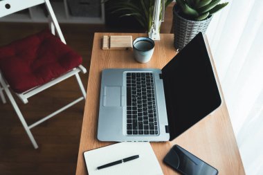 Yaratıcı bir ev ofisinde dizüstü bilgisayarı olan bir çalışma masasının üst görüntüsü. Masada uzanmak: akıllı telefon, defter, kahve fincanı, kalem, gözlük, yeşil bitkiler. Ev için çalışma kavramı