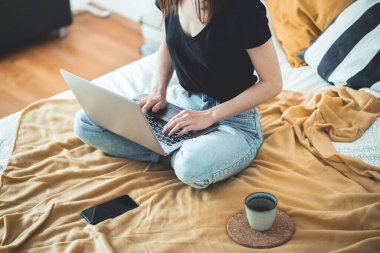 Dizüstü bilgisayarda çalışan sıradan bir kadın evdeki yatakta oturuyor. Kadın dinleniyor ve bir fincan sıcak kahve ya da çay içiyor. Laptop bilgisayar kullanıyor. Ev kavramından çalış