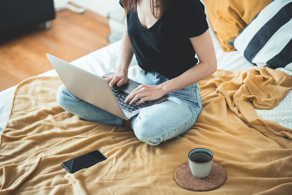 Dizüstü bilgisayarda çalışan sıradan bir kadın evdeki yatakta oturuyor. Kadın dinleniyor ve bir fincan sıcak kahve ya da çay içiyor. Laptop bilgisayar kullanıyor. Ev kavramından çalış