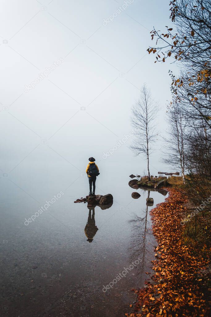 Reflection of a male backpacker standing on rock against foggy weather