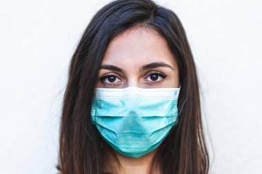 Koruyucu bir yüz maskesi takan ve kameraya bakan genç bir kadının portresi, salgının sona ermesi konusunda iyimser görünüyor. Coronavirus salgını ve karantina kavramı