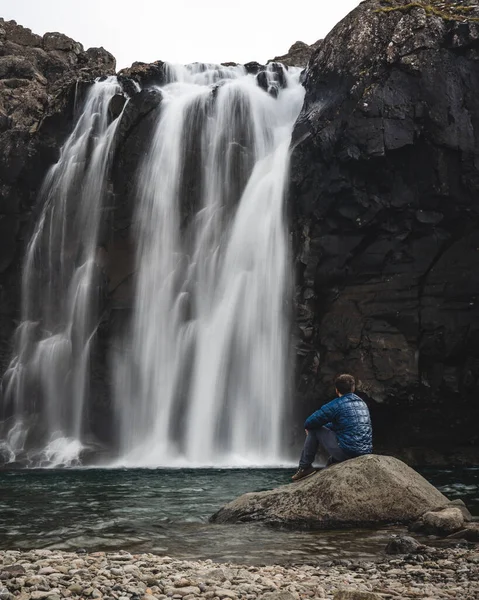 Человек, сидящий у водопада с миром — стоковое фото
