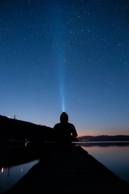 Gece gökyüzüne el feneriyle bakan adam
