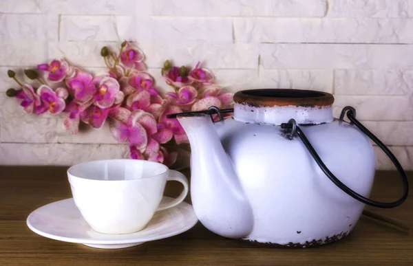 Biały czajnik z białą filiżanką kawy na tle cegły ściany i drewniany stół, w stylu retro czajniczek, piękny kwiat archidea. — Zdjęcie stockowe