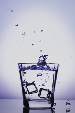 Cam içine sıçramasına buz, buz küpü bardak su, taze, soğuk su, mavi, menekşe mavi arka plan üzerinde izole düştü.