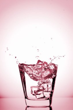 Cam içine sıçramasına buz, buz küpü bardak su, taze, soğuk su, gül, kırmızı, pembe, mor arka plan izole düştü.