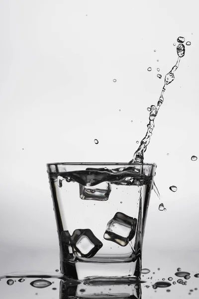 Ijsblokjes spatten in glas, daalde ijsblokje in een glas water, vers, koud water, geïsoleerd op witte, blauwe, zilveren, blauwe achtergrond. — Stockfoto