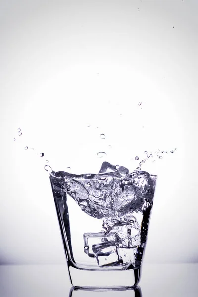 Cubos de hielo salpicando en vidrio, cubo de hielo caído en un vaso de agua, agua dulce y fría, aislado en blanco, azul, plata, fondo azul . —  Fotos de Stock