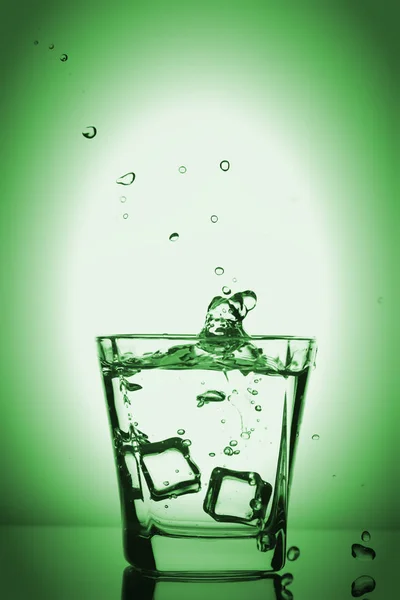 Παγάκια εκτινάξεις σε ποτήρι, παγάκι έπεσε σε ένα ποτήρι νερό, φρέσκο, κρύο νερό, απομονώνονται σε πράσινο φόντο. — Φωτογραφία Αρχείου