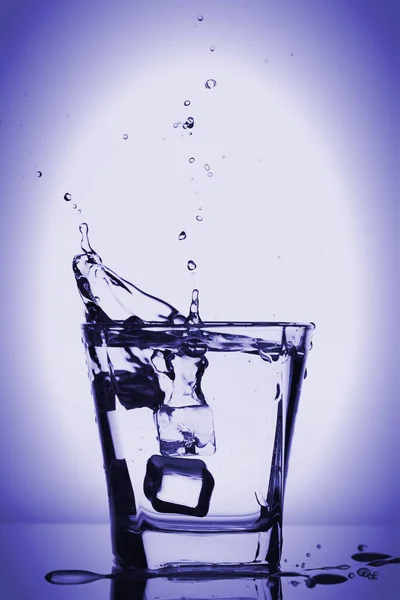 Cubos de hielo salpicando en vidrio, cubo de hielo caído en un vaso de agua, agua dulce y fría, aislado en azul violeta, fondo violeta . —  Fotos de Stock