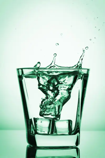 Cubos de hielo salpicando en vidrio, cubo de hielo caído en un vaso de agua, agua dulce y fría, aislado en verde, verde fondo azul . —  Fotos de Stock