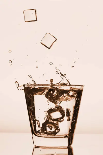 Παγάκια εκτινάξεις σε ποτήρι, παγάκι έπεσε σε ένα ποτήρι νερό, φρέσκο, κρύο νερό, απομονώνονται σε αυξήθηκε, ροζ, κόκκινο φόντο. — Φωτογραφία Αρχείου
