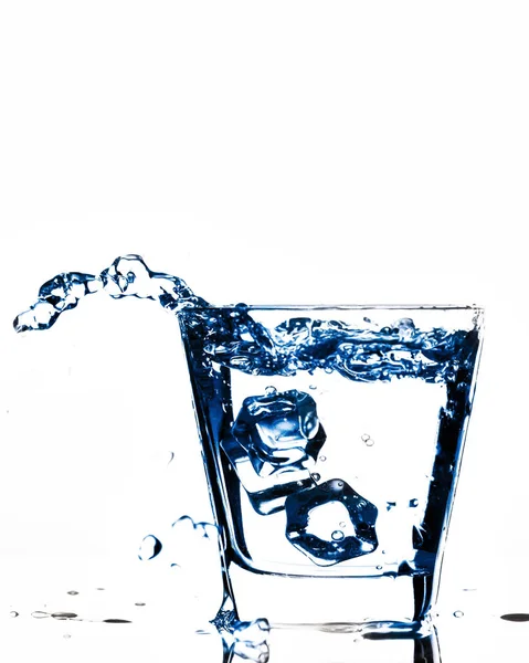 Ijsblokjes spatten in glas, daalde ijsblokje in een glas water, vers, koud water, geïsoleerd op wit, blauw, caribian blauwe achtergrond. — Stockfoto