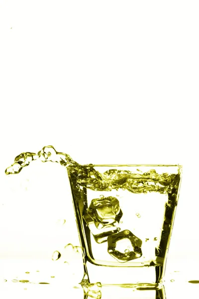 Παγάκια εκτινάξεις σε ποτήρι, παγάκι έπεσε σε ένα ποτήρι νερό, φρέσκο, κρύο νερό, απομονώνονται σε φόντο κίτρινο, χρυσό, χάλκινο. — Φωτογραφία Αρχείου