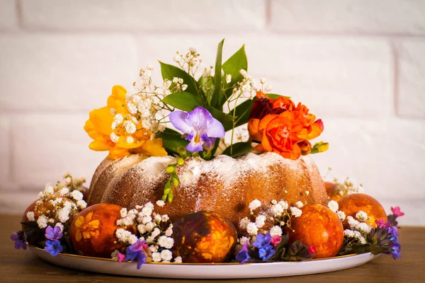 Doğu Fuar Doğu kek, renkli Doğu yumurta ve menekşe kardelen frezya çiçek ahşap masa ve beyaz tuğla arka plan ile. Mutlu Doğu, vintage Rus plaka.