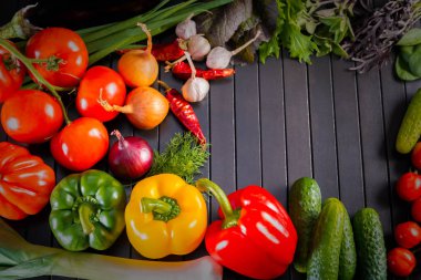 Fuar yakın çekim taze organik sebze, çeşitli ham organik sebzeler, kırmızı biber ve domates, salatalık, soğan ve sarımsak, siyah ahşap masa ile kompozisyon.