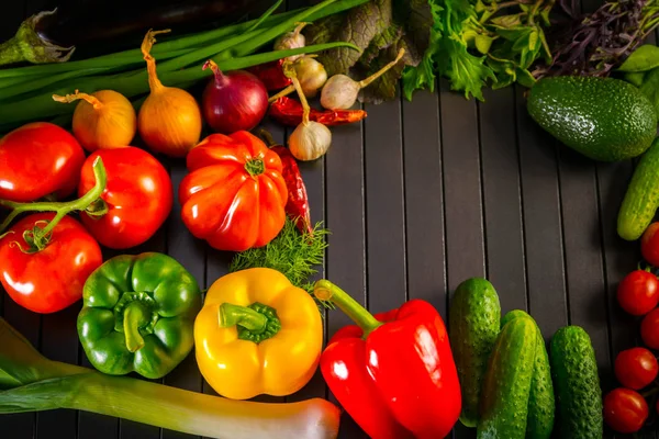 Exposition close up de légumes frais bio, composition avec assortiment de légumes crus bio, poivron rouge et tomate, concombre, oignon et ail, sur table bois noir . Images De Stock Libres De Droits