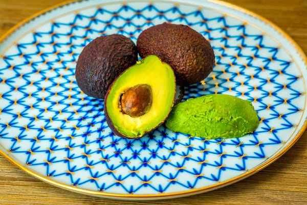 Плоды авокадо на винтажной русской фарфоровой тарелке, на деревянном столе . — стоковое фото