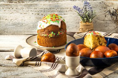 Ahşap tabakta Paskalya yumurtaları, güzel lale çiçekleri ve beyaz ahşap arka planda Paskalya pastası sergisi..