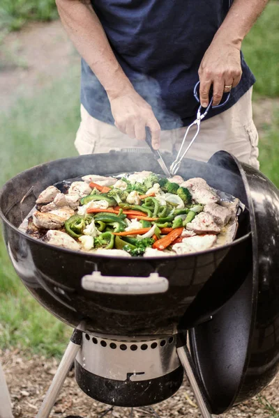 Man grilling vegetables and pork chops on a charcoal grill in the backyard in summer