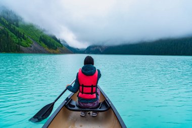 Woman paddling a canoe through Lake Louise clipart